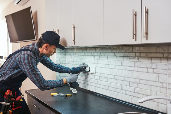 Electricity protection. Side view of young handyman setting new sockets with perforator at the kitchen
